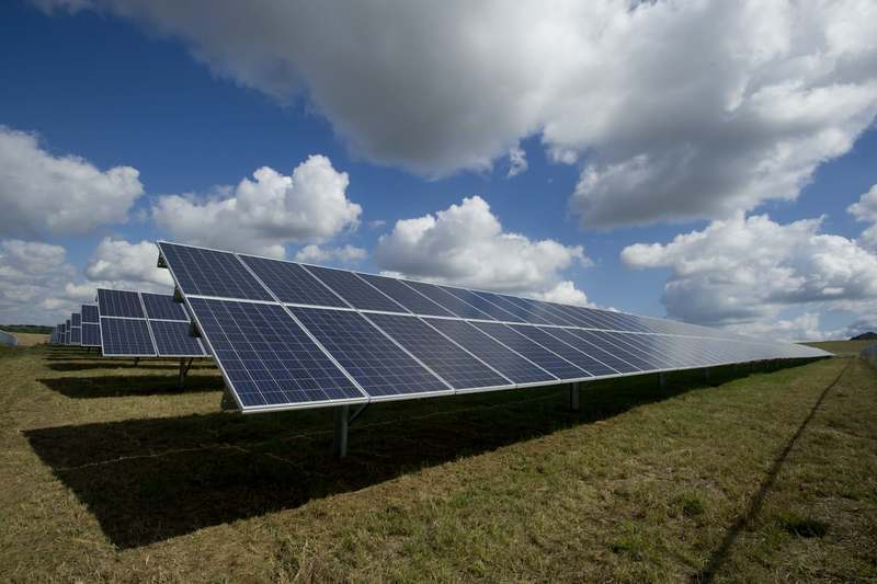 Rows of commercial solar panels on a green field under a blue sky